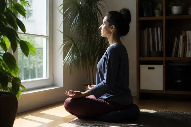 Personne assise en position confortable sur un coussin de méditation près d une fenêtre lumineuse