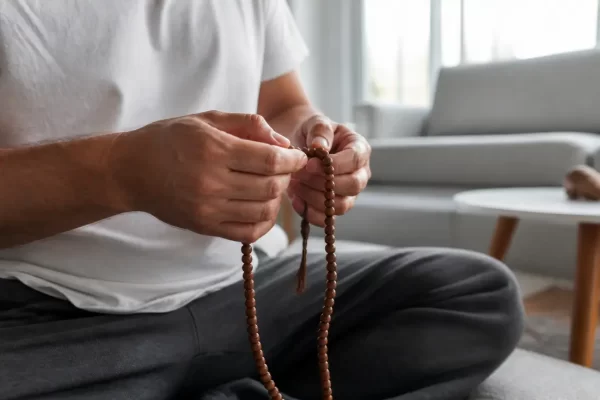 Mains tenant un mâlâ traditionnel pour réciter un mantra bouddhiste lors d'une séance de méditation à domicile.