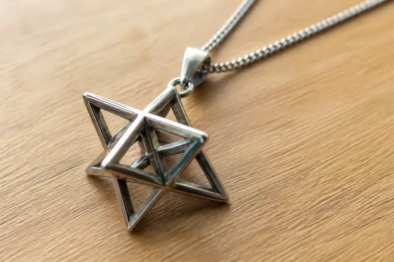 Pendentif en forme de Merkaba posé sur une table en bois illustrant le symbole géométrique statique
