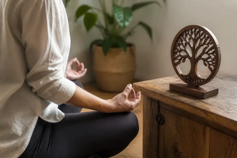 Une personne assise en méditation regarde un petit objet sculpté en bois posé devant elle sur une table.